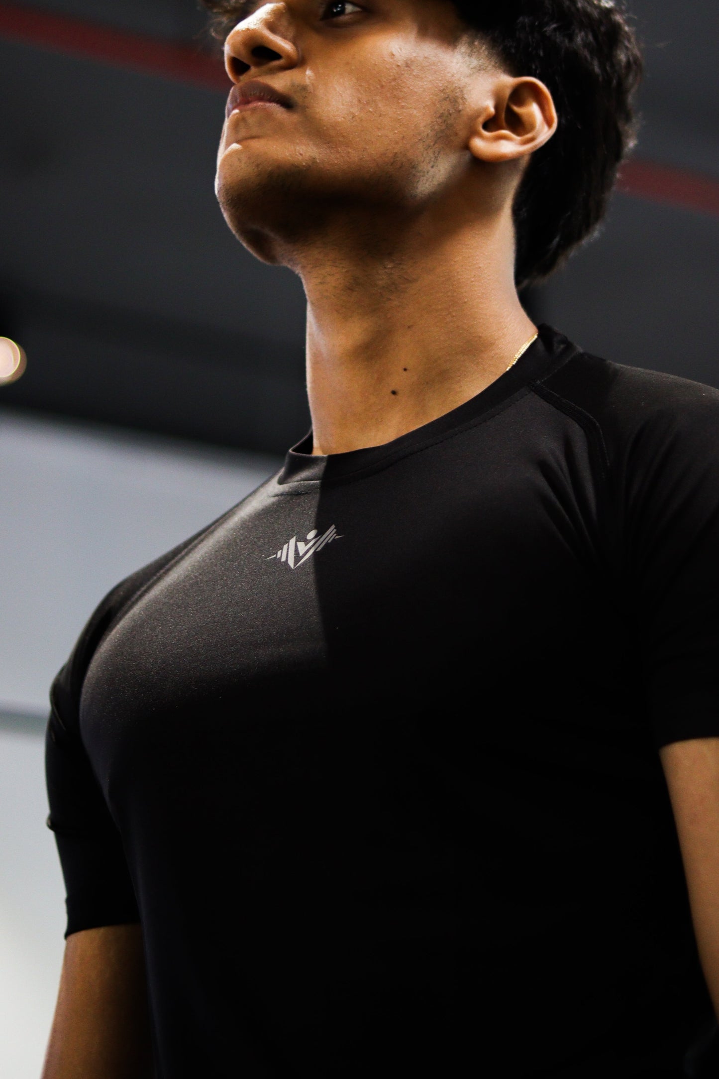 Person wearing a black t-shirt in an indoor setting with lights on the ceiling.